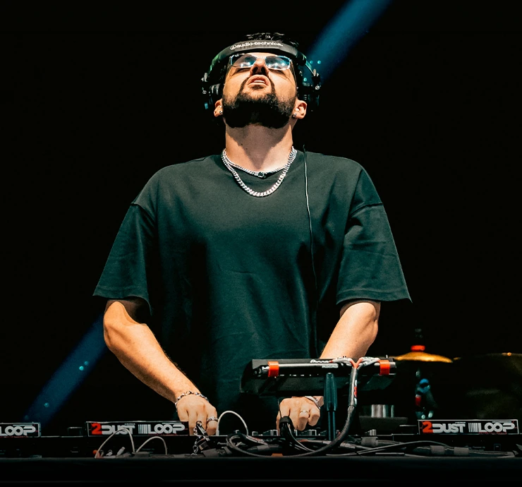 Karpan playing a DJ set, hands on the mixer under a single blue spotlight.